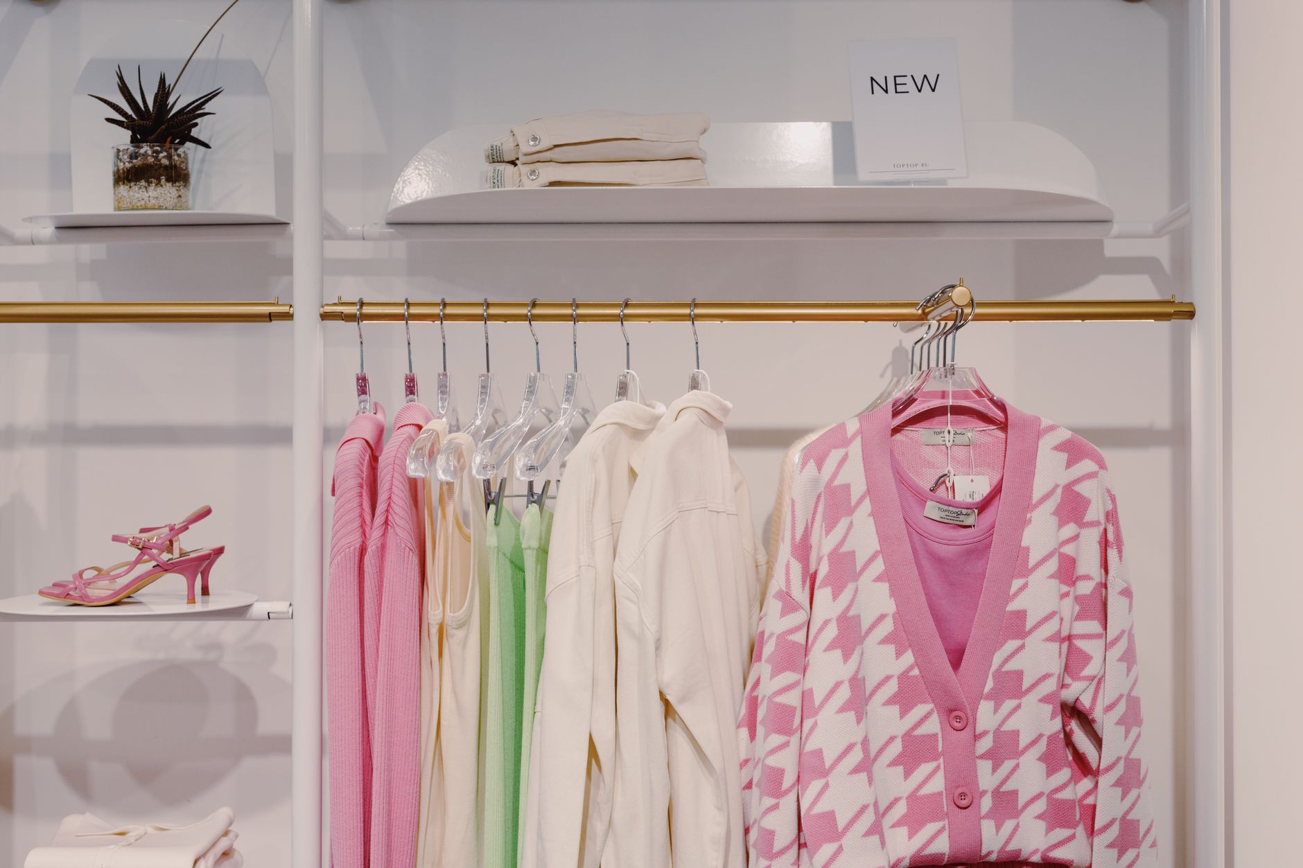 Stylish women's clothing on rack featuring pink cardigan and green dress inside a boutique